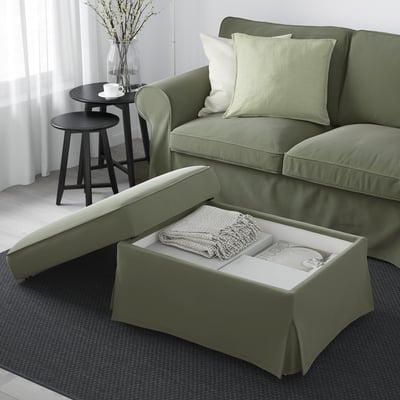 Modernes Wohnzimmer mit grünem EKTORP-Sofa und offenem Aufbewahrungshocker, freizügiger Decke und Büchern auf Teppich neben schwarzem Beistelltisch mit Tasse und Vase.