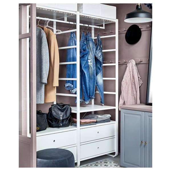 Ein weißer Kleiderschrank ELVARLI mit Regalen und Schubladen. Es bietet Platz für Jeans, Mäntel und Taschen. Eine Lampe und ein Spiegel befinden sich in der Nähe.
