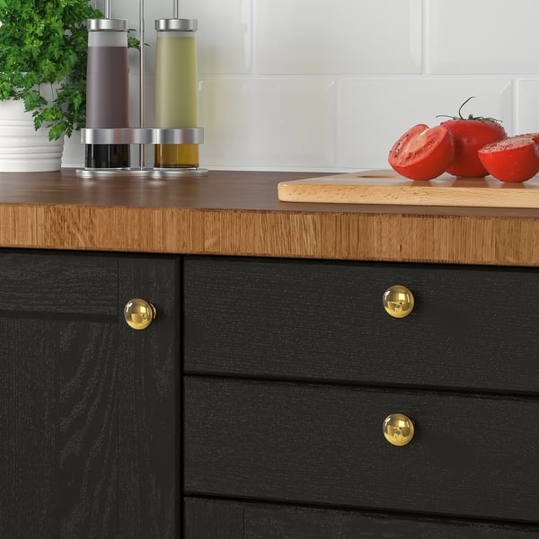Holzschublade mit goldenen Knöpfen, die Tomaten auf einem Schneidebrett halten, Salz- und Pfeffermühlen auf heller Holztheke.