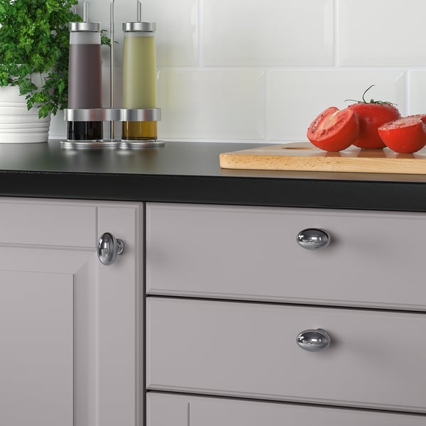 Küchenschrank mit verchromten ENERYDA-Knöpfen. Auf der Arbeitsplatte befinden sich in Scheiben geschnittene Tomaten und Ölspender.