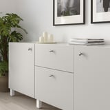 Weißer Schrank mit Knöpfen; Kerzen und Pflanze obendrauf; gerahmte Kunst dahinter.