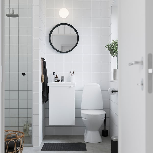 Modernes Badezimmer mit weißem ENHET-Schrank, rundem Spiegel, WC und Pflanzen. Das glänzende Gerät lässt sich hoch montieren und passt in enge Räume.