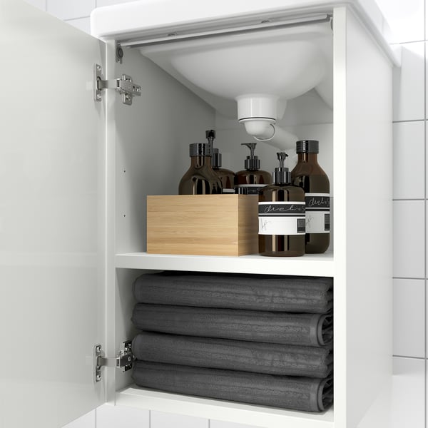 Weißer Schrank unter dem Waschbecken mit Handtüchern, Holzkiste und Flaschen.