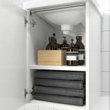 Weißer Schrank unter dem Waschbecken mit Handtüchern, Holzkiste und Flaschen.