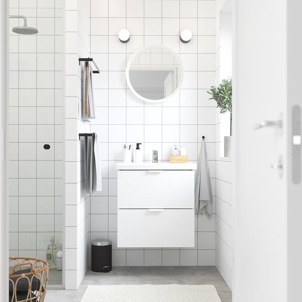 Modernes weißes Badezimmer mit wandmontiertem Waschtisch, rundem Spiegel und grauer Fußmatte.