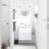 Modernes weißes Badezimmer mit wandmontiertem Waschtisch, rundem Spiegel und grauer Fußmatte.