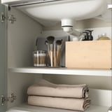 Ordentlich organisierter Badezimmerschrank mit Handtüchern, Make-up-Pinseln und anderen Toilettenartikeln auf Regalen.