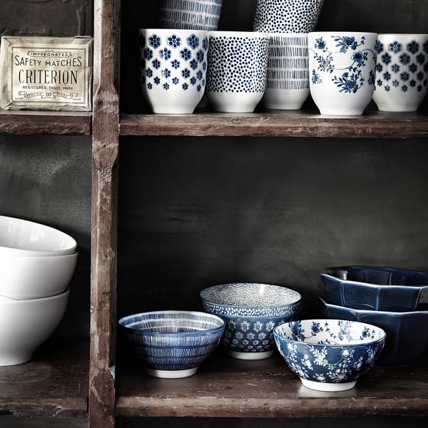 Kollektion von blauen und weißen Keramikbechern und -schalen mit floralen und geometrischen Mustern, die auf rustikalen Holzregalen angeordnet sind.