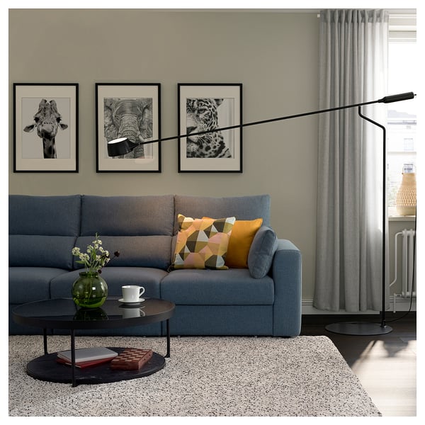 Modernes Wohnzimmer mit blauem Sofa, bunten Kissen, Couchtisch aus Glas, grüner Vase, Kunstwerk, Stehlampe.