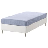 Ein weißes Polsterbett mit blauer Matratze, feste Federstütze.