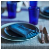 Tischdekoration mit blauem Teller, gefalteter Serviette, Gläsern, Besteck.