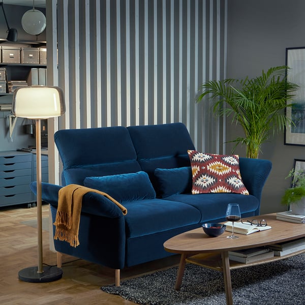 Blaues Samtsofa mit Kopfstützen und Holztisch vor dunkler Wand mit Pflanzen.
