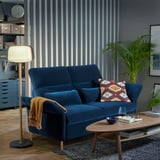 Blaues Samtsofa mit Kopfstützen und Holztisch vor dunkler Wand mit Pflanzen.