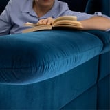 Eine Person, die ein Buch liest, während sie bequem auf einem blauen FAMMARP-Sofa sitzt.