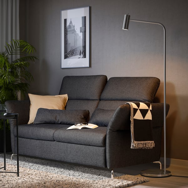 Modernes Wohnzimmer mit dunkelgrauem FAMMARP-Sofa, Kissen, Decke, Stehlampe und Pflanze.