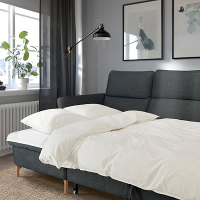 Modernes graues FAMMARP-Sofa, weiße Bettwäsche, verstellbare Lampe, Wandkunst dekorieren, Topfpflanze auf der Fensterbank.