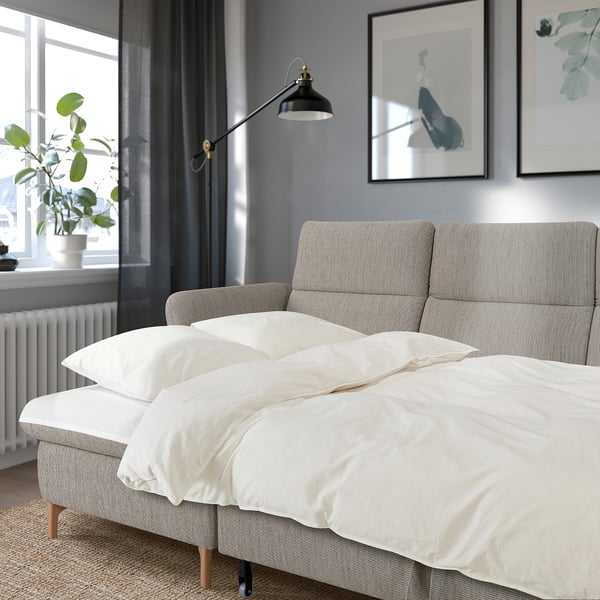 Graues FAMMARP-Sofa in gemütlichem Raum mit Kunst, verstellbaren Kopfstützen, großen Fenstern und Pflanze.