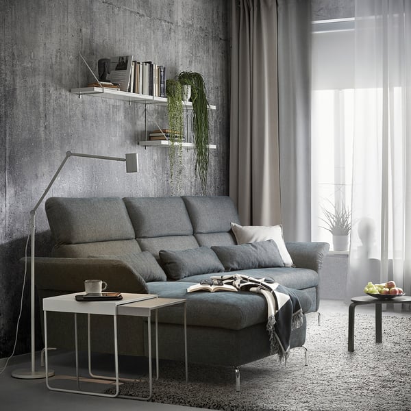 Modernes Wohnzimmer mit grauem FAMMARP-Sofa, weißen Tischen und Hängepflanzen.