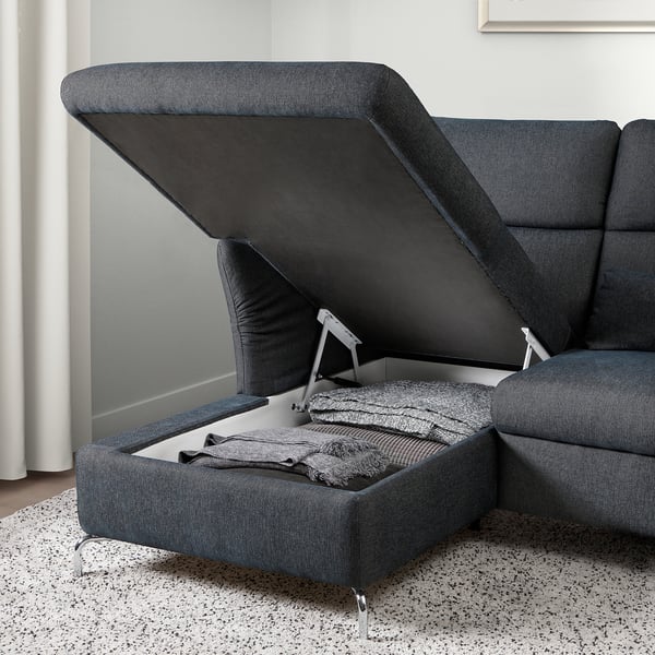 Graues Sofa mit aufklappbarem Sitz enthüllt versteckten Stauraum, der mit gefalteten Decken oder Kissen gefüllt ist.