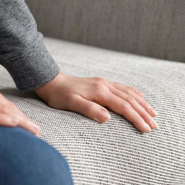 Die Hand ruht auf einem grauen Stoffsofa.