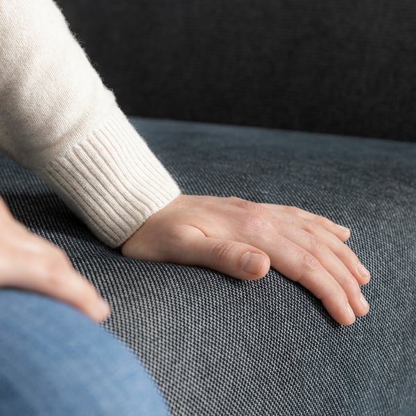 Die Hand einer Person ruht auf einem grauen FAMMARP-Sofa und zeigt den weichen, strukturierten Stoff und das moderne Design.