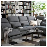 Modernes Wohnzimmer mit FAMMARP-Sofa, schwarzem Couchtisch, Bücherregal und Pflanze.