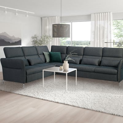 Modernes Wohnzimmer mit großem grauem FAMMARP L-förmigem Sofa, dunkelgrünen Kissen, weißem Couchtisch, großem Fenster und abstraktem Teppich.