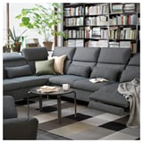 Modernes Wohnzimmer mit grauem FAMMARP-Sofa, schwarzem Couchtisch, buntem Teppich und Bücherregal voller Bücher.