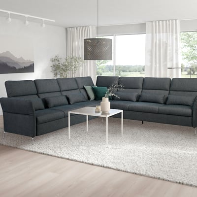 Modernes Wohnzimmer mit großem dunkelgrauem FAMMARP-Sofa, weißem Couchtisch, floralen Akzenten, großen Fenstern und trendiger Pendelleuchte.