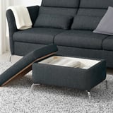 Dunkelgraues Sofa mit FAMMARP-Fußstütze, verstecktem Stauraum und verstellbaren Sitzen. Die Fußstütze zeigt eine gestreifte Decke im offenen Fach.