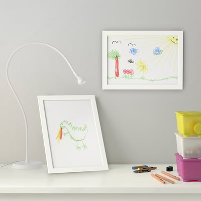 Kinderzeichnungen in weißen Rahmen auf dem Schreibtisch. Lampe, Künstlerbedarf und Abstellraum in der Nähe.