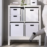 Weiße FJÄDERHARV-Aufbewahrungsboxen im Regal mit Büchern und Büromaterial, in die eine Person hineingreift.