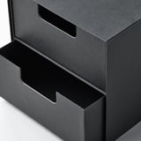 Schwarzer Mini-Aufbewahrungsschrank mit Schubladen aus strukturiertem Karton; glatte Griffe, abwechselnd offene und geschlossene Positionen, gepflegtes und modernes Design.
