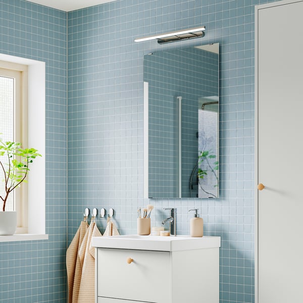 Modernes Badezimmer mit blauen Fliesen, Spiegel, Waschbecken und verchromter FLASKPOST-Leuchte darüber. Das verstellbare, minimalistische Design sorgt für blendfreie Beleuchtung.