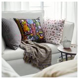 Gemütliches Sofa mit bunten Kissen, gefalteter Decke und Kaffeetasse; Mischung aus Mustern und Texturen.