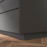 Grauer FÖRBÄTTRA Küchenschranksockel auf Holzboden.