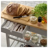 Grauer FÖRHÖJA Küchenwagen mit Holzplatte für Brot, Messer, Nüsse, Pfeffer. Schublade mit Tüchern und Besteck, Regale mit Lebensmittelgläsern.