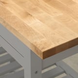 Nahaufnahme einer glatten, gut gearbeiteten Tischplatte aus hellem Holz auf robusten weißen Metallbeinen.