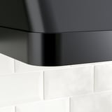 Schwarze, moderne Dunstabzugshaube mit glatten Kurven, die über weißen Fliesen montiert sind.
