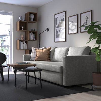 Modernes Wohnzimmer mit FRIHETEN-Sofa, Kissen, Couchtisch, Bücherregal und Wandkunst.