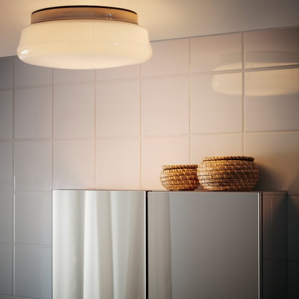 Ein modernes Badezimmer mit einer runden Deckenleuchte, die diffuses Licht spendet, und zwei Weidenkörben auf einem Schrank.