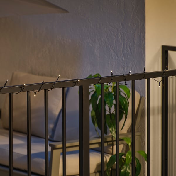 Schwarzes Metallgeländer mit warmweißen LED-Leuchten, die den Außenbereich erhellen. Im Hintergrund sind eine Pflanze und Gartenmöbel zu sehen.