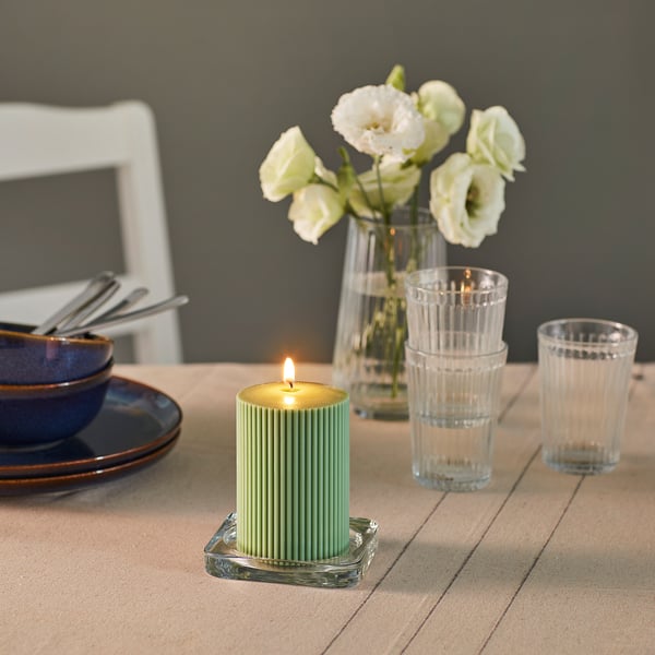 Ein Tisch mit einer brennenden Kerze, Tellern, Gläsern und einer Vase mit Blumen. Die Kerze sorgt für stimmungsvolles Licht.