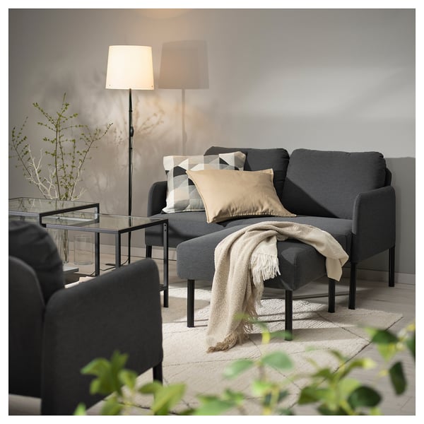 Gemütliches graues Sofa mit neutralen Kissen, drapierter Decke und Stehlampe, das einen modernen Wohnraum schafft.