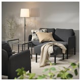 Gemütliches graues Sofa mit neutralen Kissen, drapierter Decke und Stehlampe, das einen modernen Wohnraum schafft.