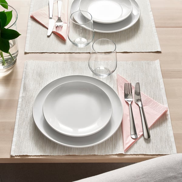 Zwei Gedecke mit weißen Tellern, Gläsern, Besteck auf geflochtenen Tischsets für elegantes Essen.