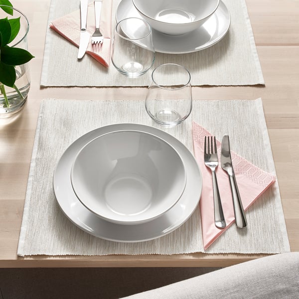 Zwei gedeckte Tische mit weißen Tellern, Schüsseln, Gläsern, Besteck und rosa Servietten auf beigen Tischsets.