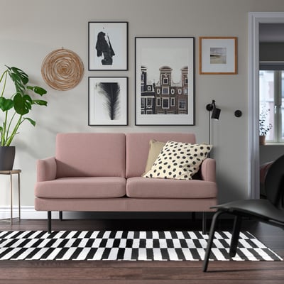 Modernes Wohnzimmer mit rosa GRILLSTORP-Sofa, Kunst, Pflanze und kariertem Teppich.