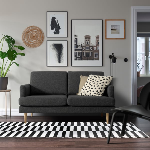 Modernes Wohnzimmer mit GRILLSTORP-Sofa, schwarz/weißem Teppich, Kunst, Lampe, Pflanze.