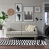 Modernes Wohnzimmer mit grauem GRILLSTORP 2-Sitzer-Sofa, Kunstwand, Teppich und Pflanze.